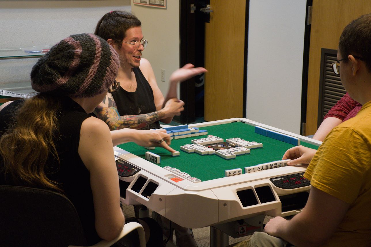 A player discards a tile while another gestures to the players.
